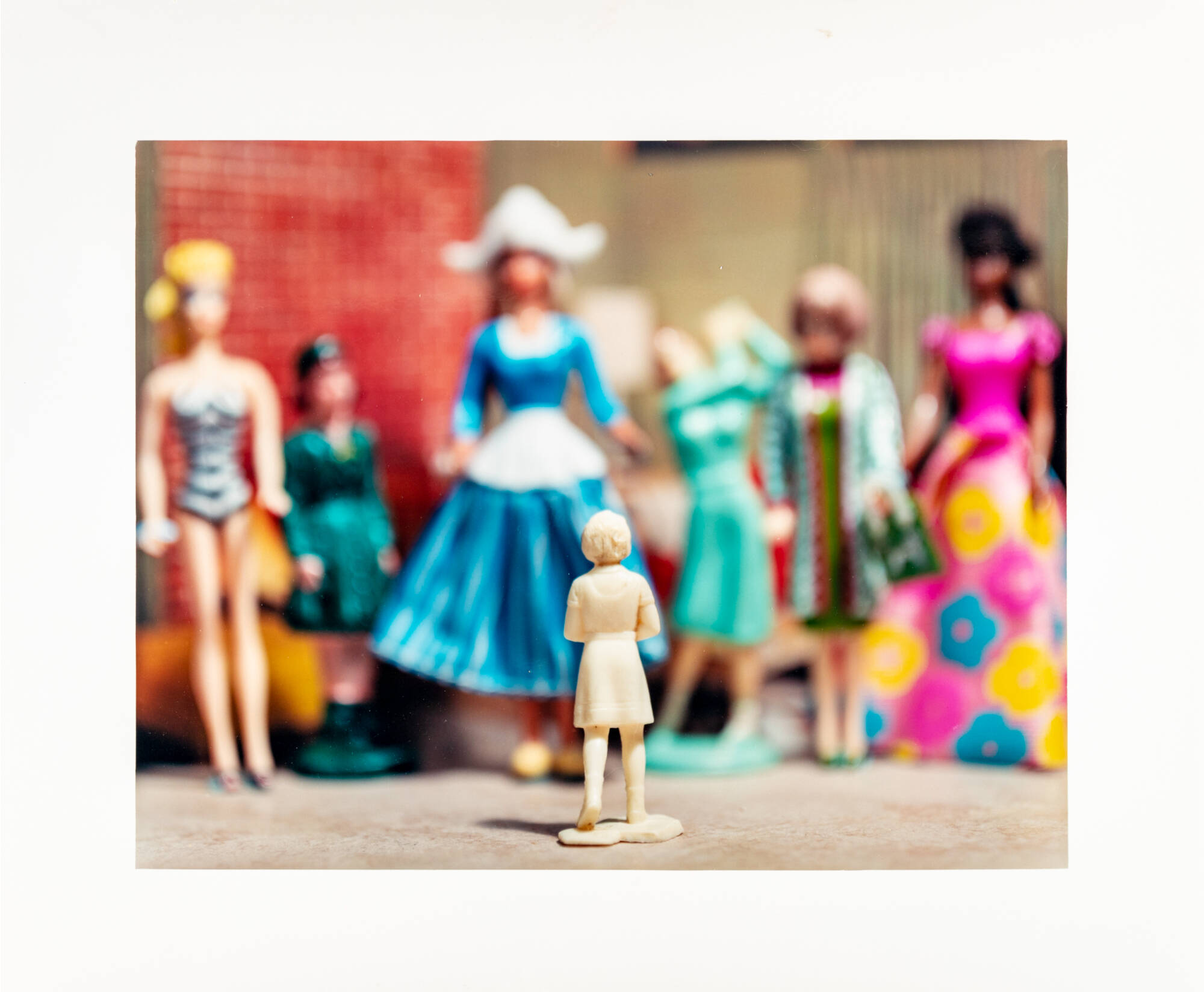 A photo of a small white figurine in focus surrounded by larger out-of-focus dolls.